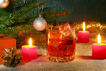 christmas decoration with glass of whiskey or cognac, christmas candles, tree and gift box on a sparkling background. New Year decoration.