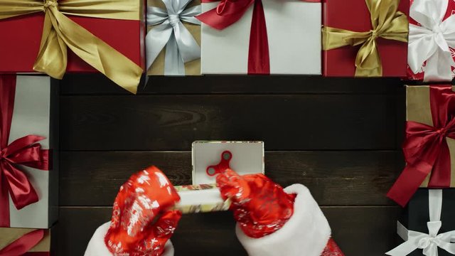 Santa spins with fidget spinner and puts it in gift box on Xmas table, top down shot
