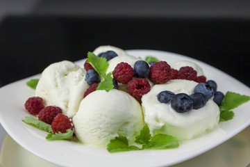 vanilla ice cream with raspberries, blueberries and mint leaves on white plate