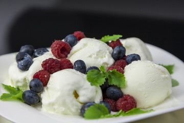ice cream with raspberries, blueberries and mint leaves on white plate against black background