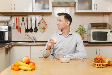 Handsome caucasian young business man in plaid shirt having breakfast, sitting at table, eating cereals with milk on light kitchen. Dieting concept. Healthy lifestyle. Cooking at home. Prepare food.