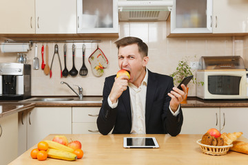 Handsome young business man in suit, shirt, having breakfast, sitting at table with tablet, talking...