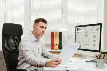 Serious and engrossed business man in shirt sitting at the desk, working at computer with modern...