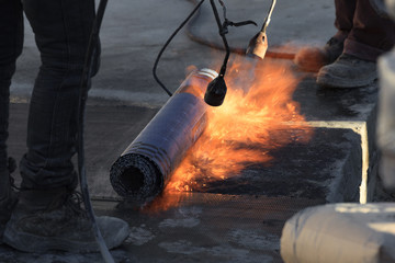 Laying of roofing felt from the roll with a flame from the burner close-up. - obrazy, fototapety, plakaty