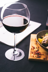 glass of red wine in front of freshly cooked meat and potatoes freshly cooked meat and potatoes in metal pan on cutting board