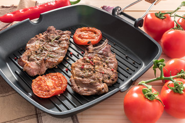 Grilled steak on grill pan with tomatoes on wooden background