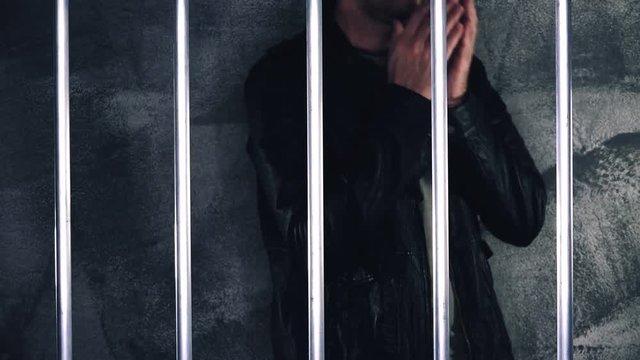 Depressed handcuffed man behind prison bars