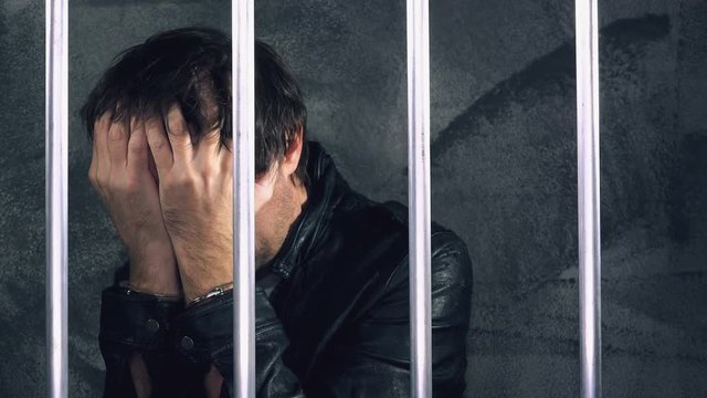 Depressed handcuffed man behind prison bars