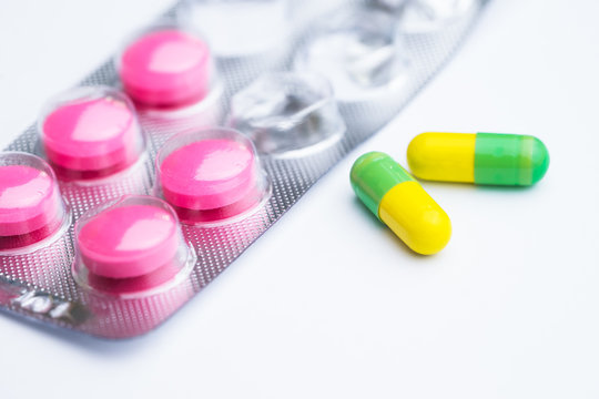Yellow and green capsule with used magenta tablets, medical pills in silver foil pack on white background.