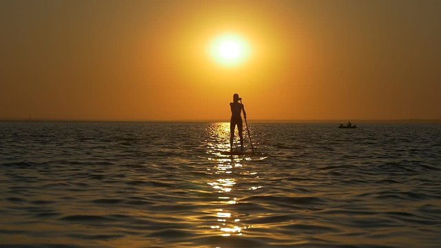 Silhouette of a woman on a standup paddle board at orange sunset