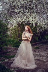 Beautiful happy young woman with red hair enjoying smell in a flowering spring garden