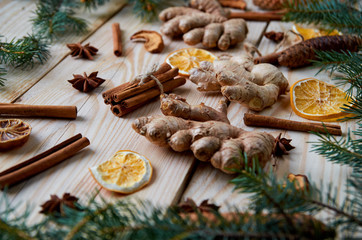 Fototapeta na wymiar Ginger on the wooden background with traditional spices ingredients for Christmas bakery or mulled wine dried orange, cinnamon, anise. Decorated with blurred Christmas tree branches. Holiday mood