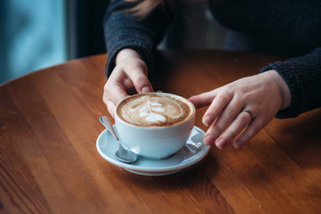 Beautiful young woman enjoying coffee cappuccino with foam near window in a cafe