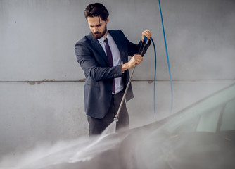 Serious focused attractive bearded man in suit washing his car at the manual car washing...