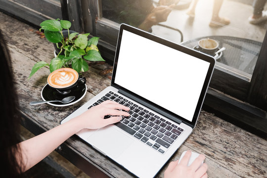 Mockup Image Of Business Woman Using And Typing On Laptop With Blank White Screen And Coffee Cup On Glass Table In Modern Loft Cafe, Soft Focus On Vintage Wooden Table.