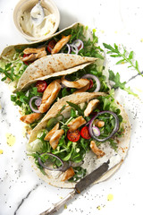 Unwrapped tortilla with fresh salad and roasted chicken and a bowl of sauce. Top view shot. Gourmet conception.