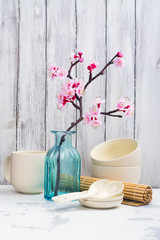 Japanese utensils, dinnerware, chopsticks and branch of blooming sakura on white asian background