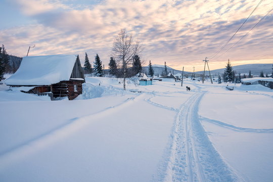 The ski track leads to the outskirts of the village with a hut in the foreground, at sunset.