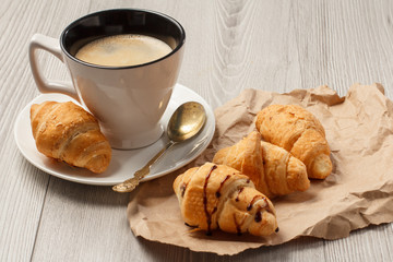 Cup of black coffee with fresh croissants on wrapping paper