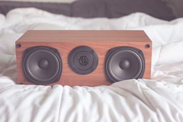 Wood speaker on white bed. Pastel style filtered photo