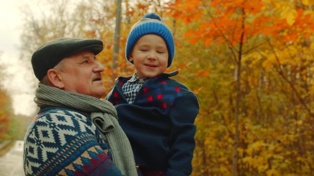 Happy little boy is hugging his grandfather in the autumn park