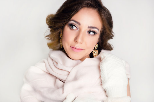 Winter image of a woman in gloves and a scarf. Professional make-up and styling. Beautiful girl with a delicate smile on a white background.