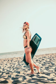 Pretty smiling Caucasian woman kitesurfer walking on the beach with her board