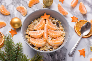 Healthy Breakfast set Granola with tangerines. Rolled Oat flakes in bowl with orange slices served like a fir tree. Marble background. Christmas food, golden ornaments, stars