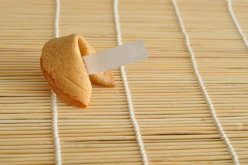 A piece of paper for a fortune displayed with a whole fortune cookie against a bamboo background