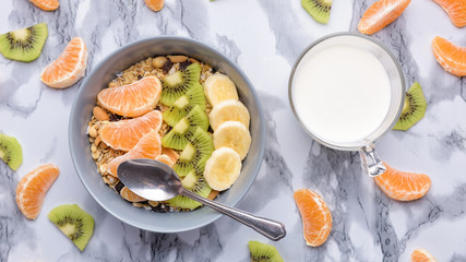 Healthy Breakfast set Granola with tangerines. Rolled Oat flakes in bowl with orange, kiwi and banana slices. Marble background. Cup of yoghurt