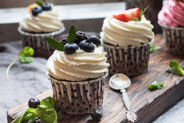 Homemade chocolate cupcakes with cheese cream, blueberry, strawberry, mint on the wooden board and vintage decoration