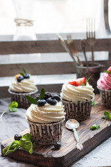 Homemade chocolate cupcakes with cheese cream, blueberry, strawberry, mint on the wooden board and vintage decoration