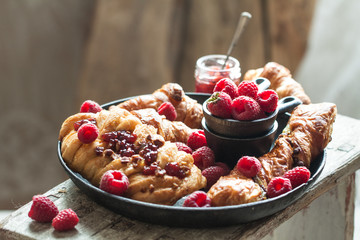 Gourmet croissant and danish buns with fresh raspberry and jam for the breakfast on the cast iron tray and wooden table