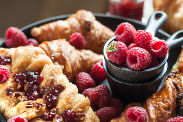 Gourmet croissant and danish buns with fresh raspberry and jam for the breakfast on the cast iron tray and wooden table