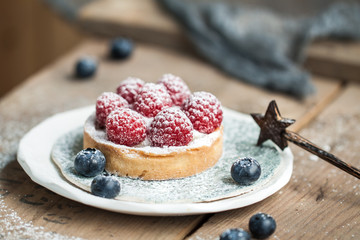 Delicious raspberry tartalet with cream and sugar puwder on the ceramic plate on the wooden background
