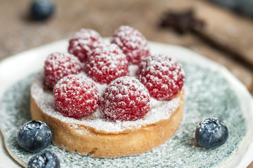 Delicious raspberry tartalet with cream and sugar puwder on the ceramic plate on the wooden background