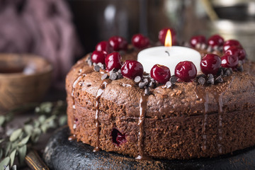 Double chocolate cherry cake with spices and big candle on the rustic background for winter holidays. Christmas and New Year decoration