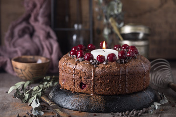 Double chocolate cherry cake with spices and big candle on the rustic background for winter holidays. Christmas and New Year decoration