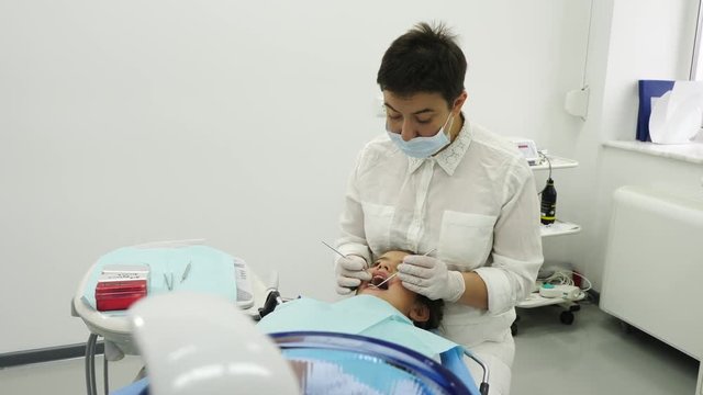 Dentist examining a teeth of little girl. Dentist using a mirror and dental proba. Camera movement. A dentist with surgey and gloves.