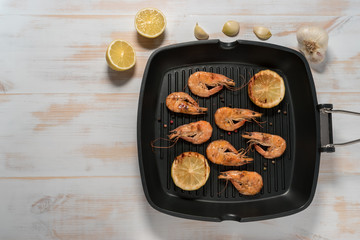 Grilled shrimps on a grill frying pan with lemon, paprika, spices and herbs. Wooden background.