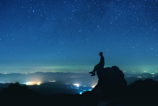 Man sits on big rock on night sky background