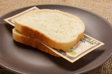 Two slices of bread with ten American dollars bill as hamburger of money on brown plate