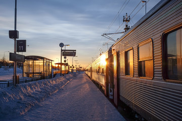 A snow-covered railway stop with a train and the sun rising