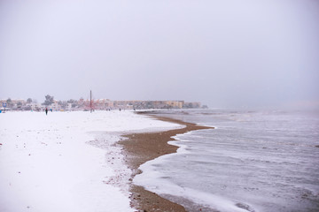 Sand beach covered with snow and stormy sea in the town Denia, Spain in winter.