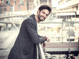 One handsome young man in urban setting in European city, standing, smiling and looking at camera