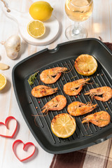 Grilled shrimps on a grill frying pan with wine, lemon, paprika, spices and herbs. Wooden background.
