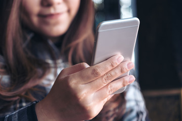 Closeup image of a beautiful Asian woman holding , using and looking at smart phone in modern cafe