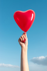 Fototapeta premium Womans hand with heart shaped balloon on background of sky.