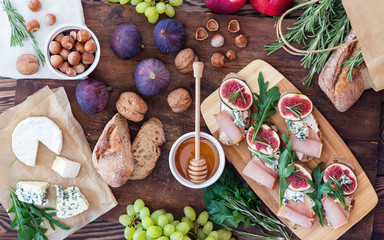 Sandwiches with ricotta, fresh figs, prosciutto, rosemary and blue cheese, walnuts and honey on rustic wooden board over black backdrop, top view. Delicious fruity breakfast.