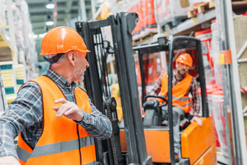 male worker and his colleague working with forklift machine in storehouse © LIGHTFIELD STUDIOS